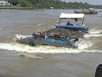 Preťažené riečne lode zdolávajú silný tok vody pod mostom (Vietnam)