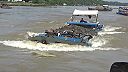 Preťažené riečne lode zdolávajú silný tok vody pod mostom (Vietnam)