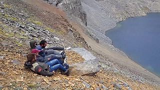 Štyria chlapi sa snažia nohami uvoľniť na brehu jazera veľký balvan (Turecko)