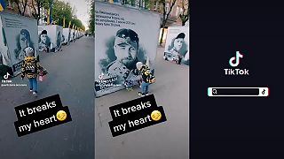 Chlapec kladie kvetiny k bilboardu svojho otca.